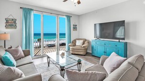 Ein Wohnzimmer mit Blick auf den Strand, einem Deckenventilator, einem Fernseher und einem blauen Schrank.