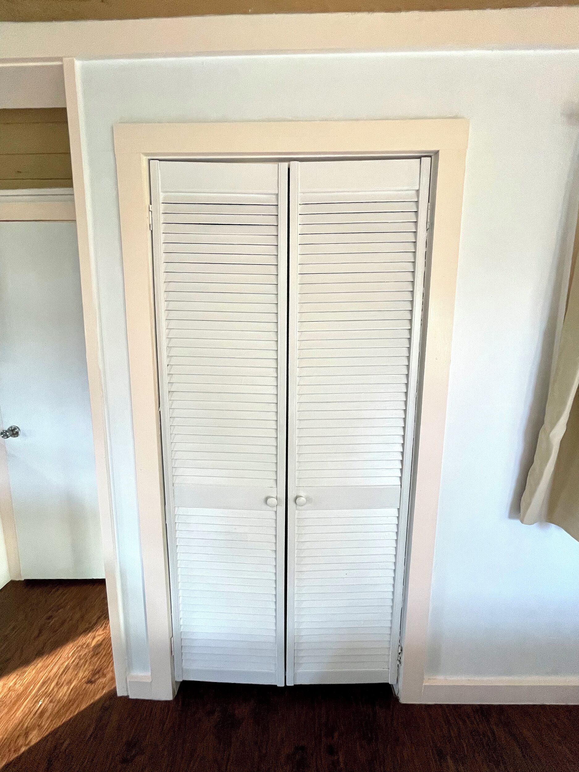 A white closet with two doors, a wooden floor, and a white wall.