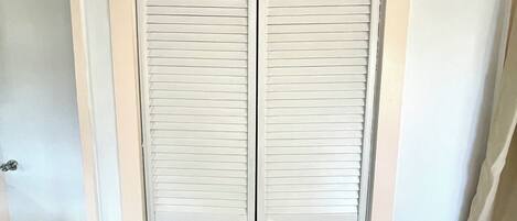 A white closet with two doors, a wooden floor, and a white wall.