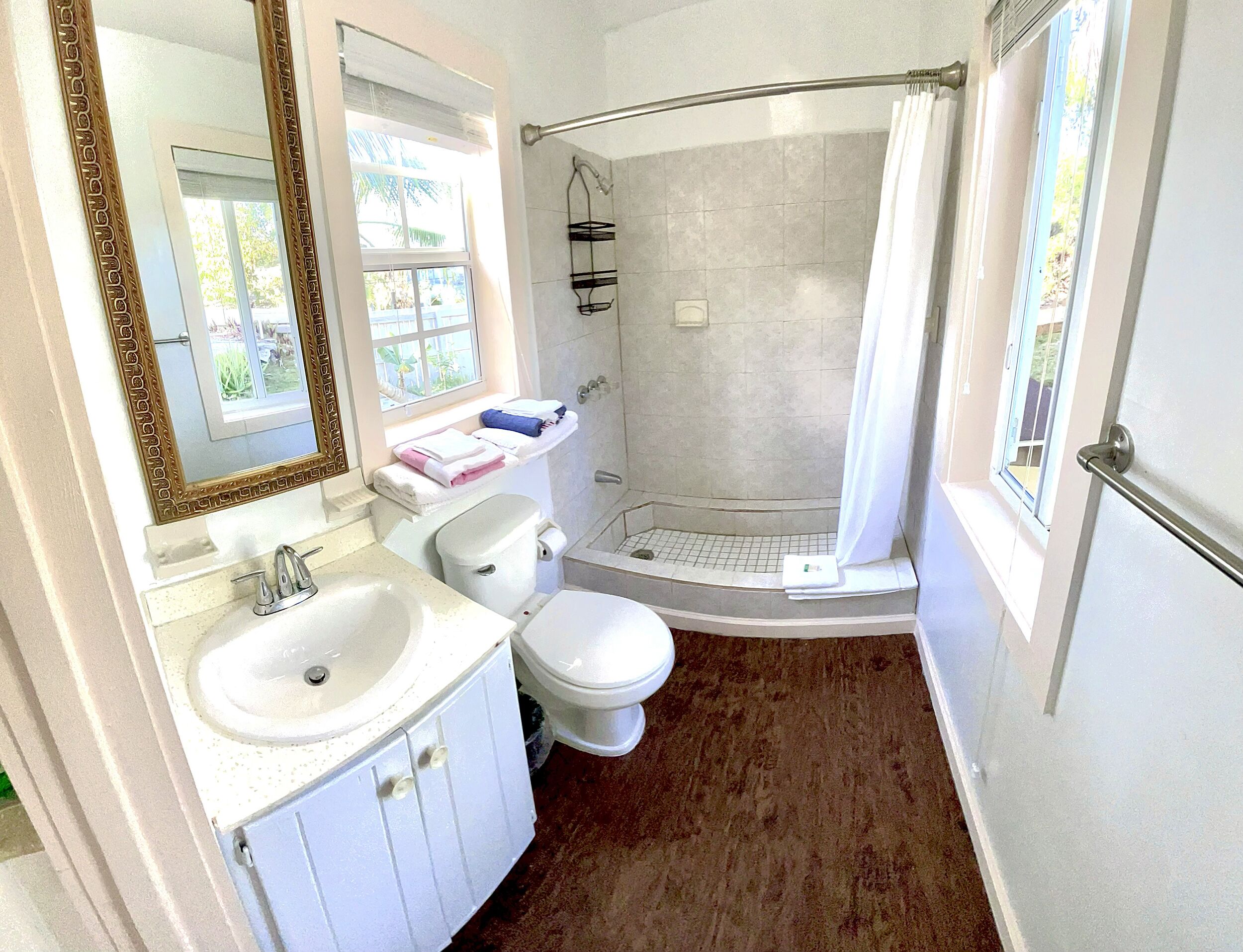 A bathroom with a shower, toilet, sink, and a large mirror.