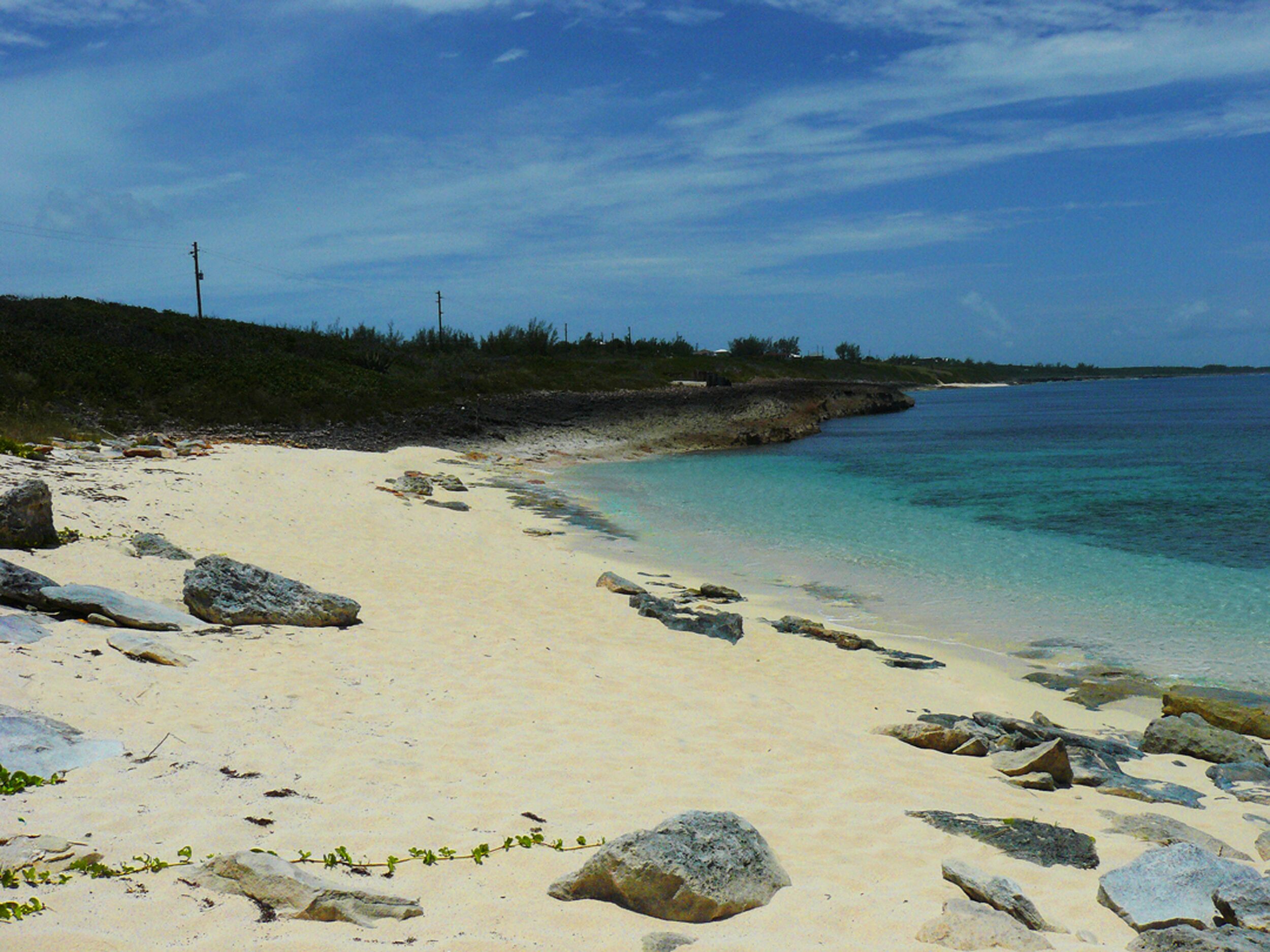 Ein Sandstrand mit großen Felsen und einem klaren, blauen Meer.