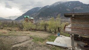 A mountainous landscape with two buildings, one with a green roof and another under construction. - GuestHouser 1 BR Cottage 4e68 (Manali)