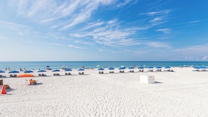 Una playa con numerosas sombrillas azules y naranjas, arena blanca y cielos azules despejados.