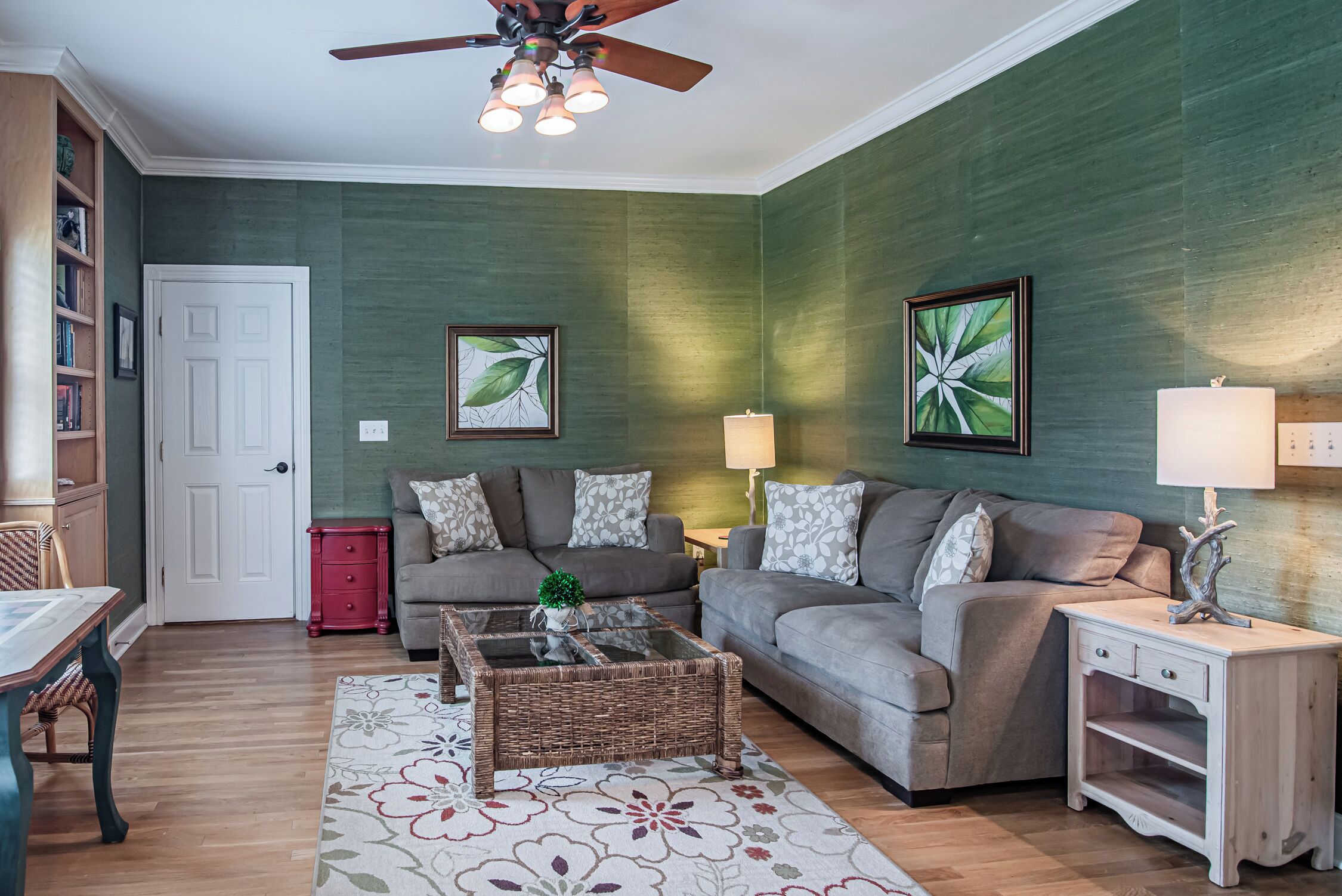 A living room with a green wall, two sofas, a coffee table, a red side table, a white side table, and a ceiling fan.