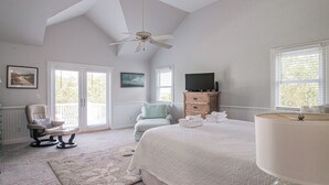 A bedroom with a large bed, a ceiling fan, a TV, and a view of the outdoors through the windows. - Legasea DeBordieu Home LegaSea Spectacular porches Close to Beach (Georgetown)