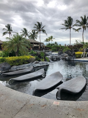 A pool area with lounge chairs, palm trees, and a waterfall. - Luxury condo in prestigious Hali'i Kai oceanfront community. Ocean bar and grill (Waikoloa Village)