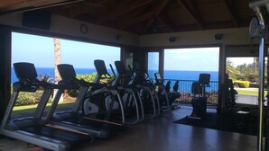 Une salle de sport équipée de tapis de course et de vélos d’exercice, offrant une vue panoramique sur l’océan.