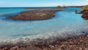 Une côte rocheuse bordée d’une eau d’un bleu limpide et d’une terre visible au loin.