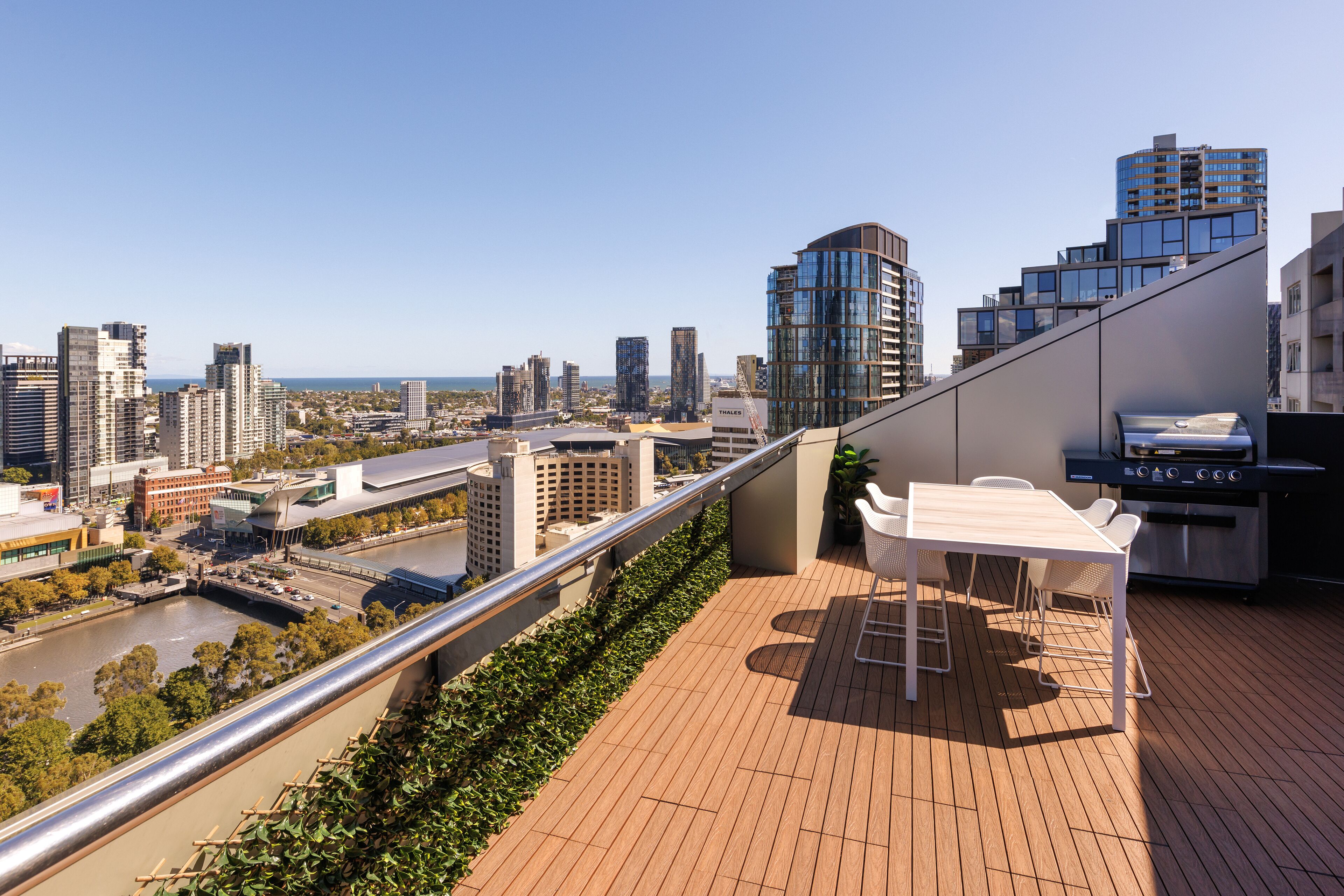 Terraço no telhado com mesa e cadeiras, vista para um horizonte urbano com edifícios modernos e um rio.