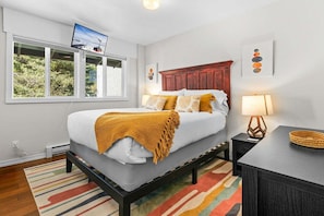 A modern bedroom with a bed, a TV, a lamp, and a view of greenery outside.