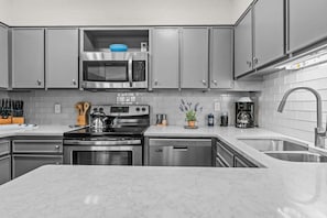 A modern kitchen with grey cabinets, a stainless steel stove, a microwave, and a coffee maker.