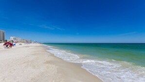 A beach with a clear sky, sandy shore, and buildings in the background. - Phoenix V 202 (Orange Beach)