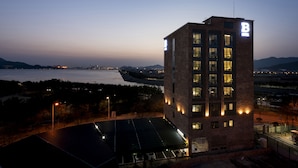 Un edificio moderno con un letrero 'B', grandes ventanales y un estacionamiento con paneles solares.