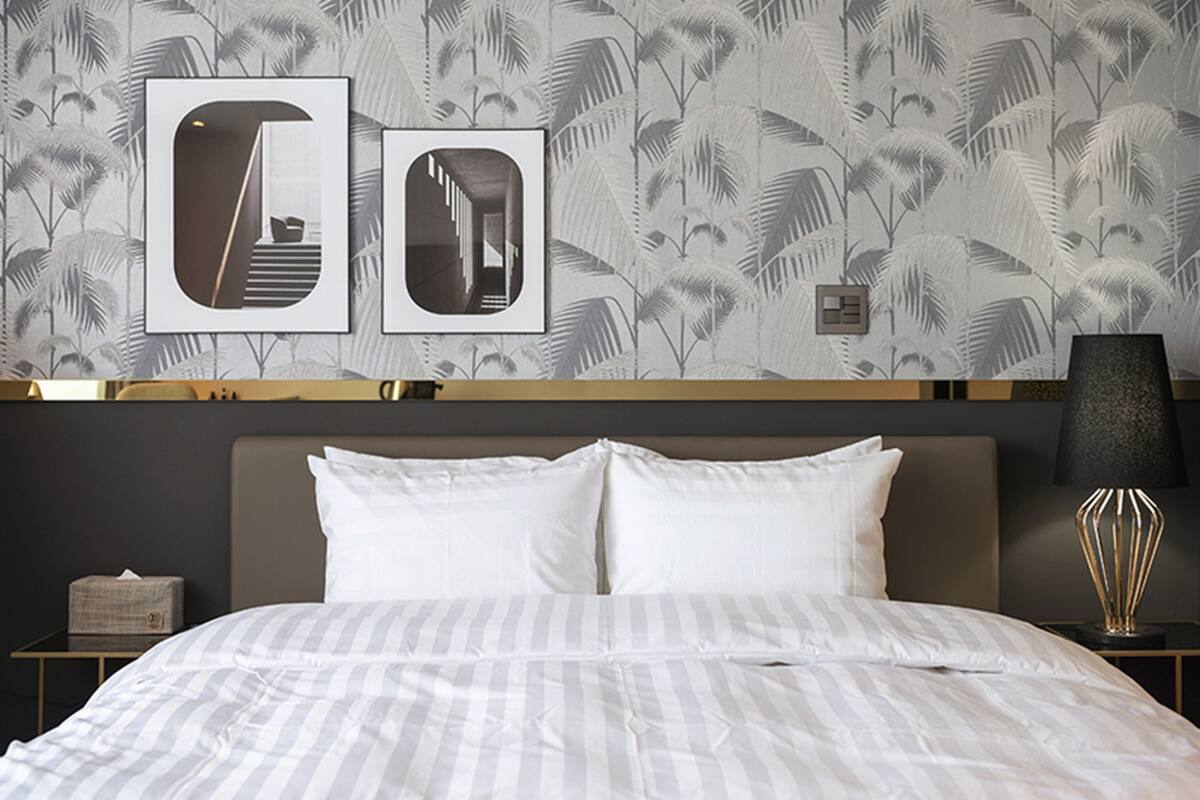 A hotel room with a bed, a nightstand, a lamp, and two framed pictures on the wall.
