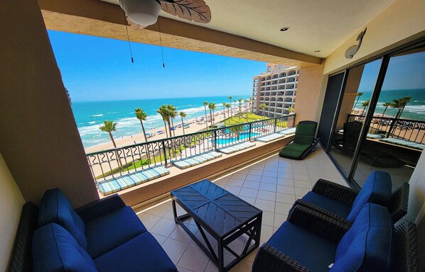 Ein Balkon mit Blick auf Strand und Meer, ausgestattet mit blauen Sofas und einem kleinen Tisch.