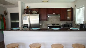 Une cuisine avec des armoires en bois, un réfrigérateur en acier inoxydable, un four à micro-ondes et une cuisinière. Il y a trois tabourets en bois au comptoir.