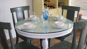 Une table ronde en verre, surmontée d’assiettes blanches et de verres à vin transparents, entourée de chaises en bois foncé.
