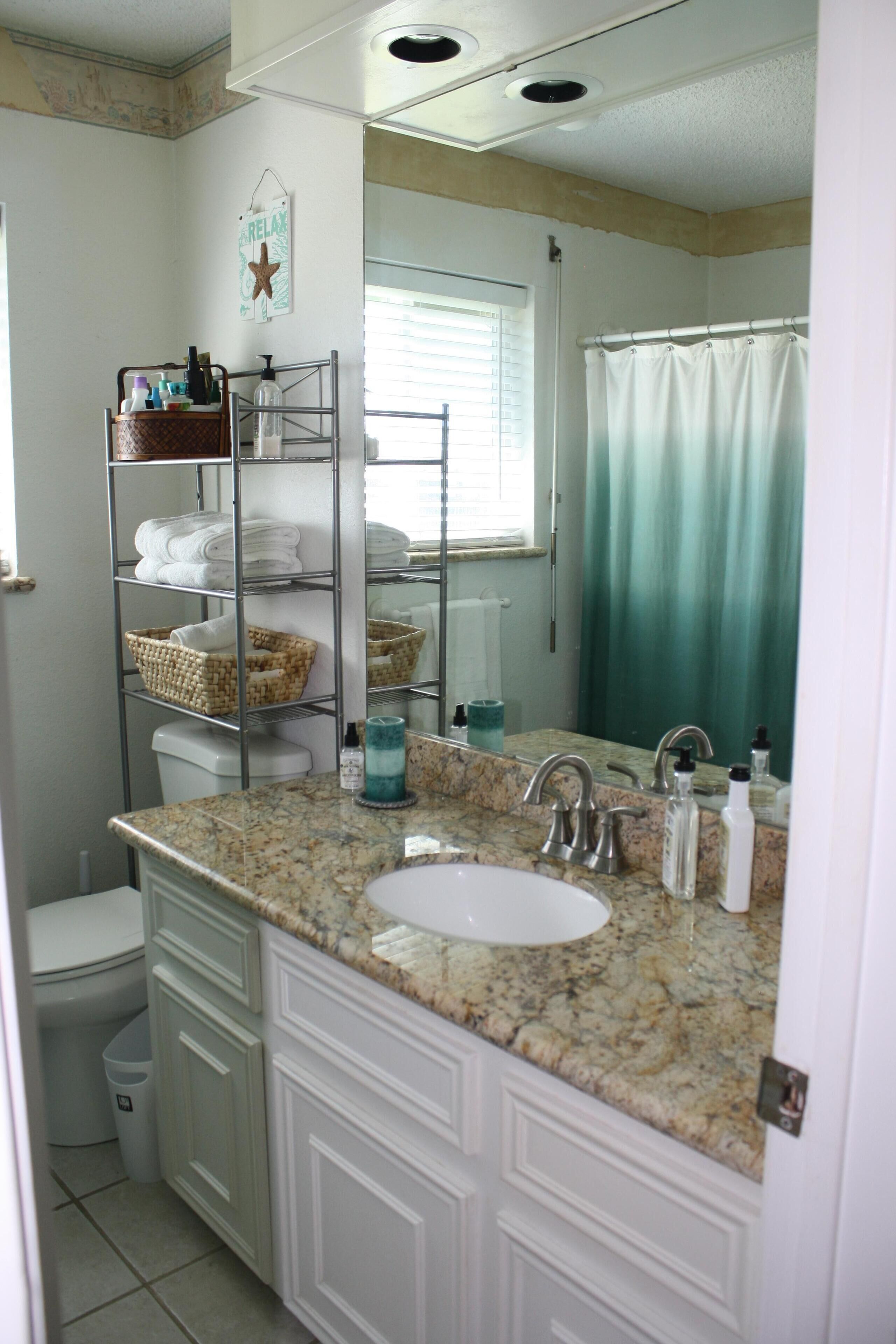 Une salle de bain dotée d’un comptoir en granit, d’un lavabo blanc et d’une étagère métallique avec des paniers.