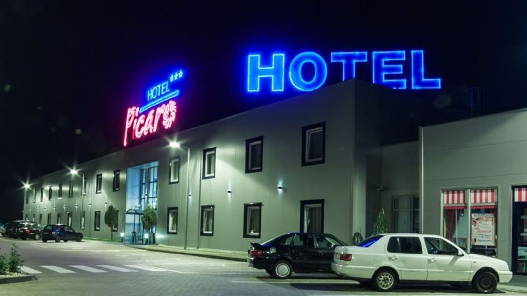 A hotel with a neon sign, a parking lot, and a street view.