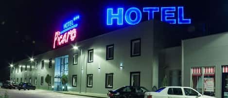 A hotel with a neon sign, a parking lot, and a street view at night.