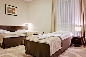 Habitació d'hotel amb dos llits, una tauleta de nit amb una làmpada, un quadre amb marc a la paret i cortines fines.