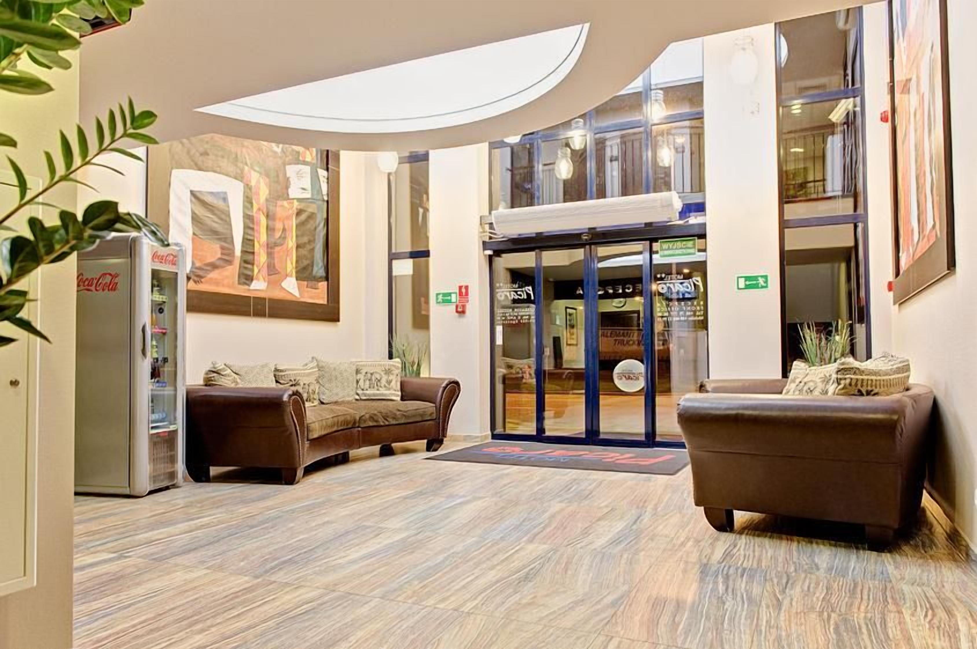 A lobby with a sofa, a Coca-Cola refrigerator, and a glass door entrance.