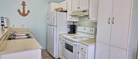 A compact kitchen with white cabinets, a stove, and a sink.