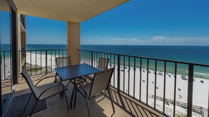 A balcony with a table and chairs overlooking a beach with umbrellas and people.