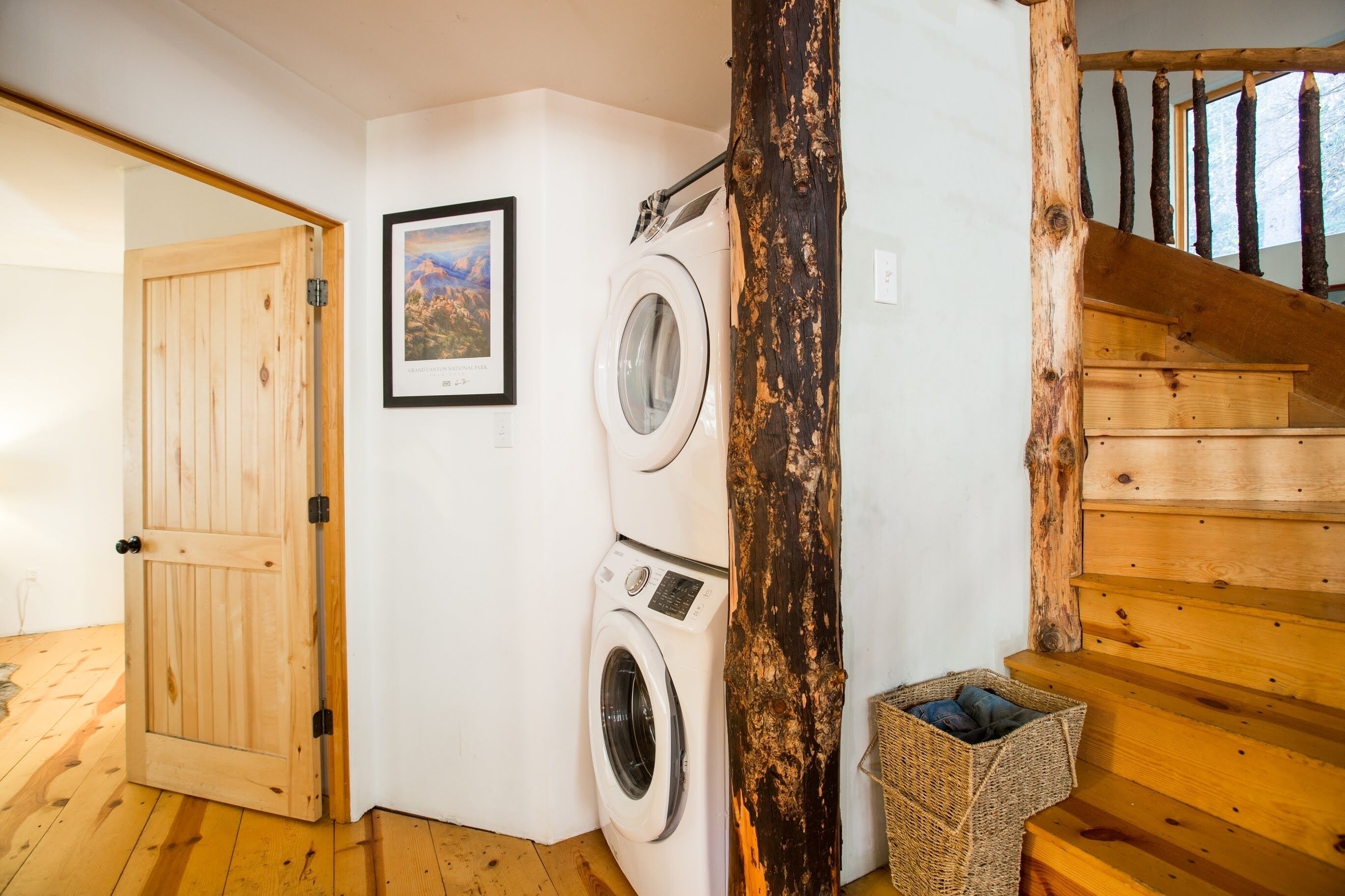 A laundry area with a washing machine, a wooden door, a framed picture, and a staircase.