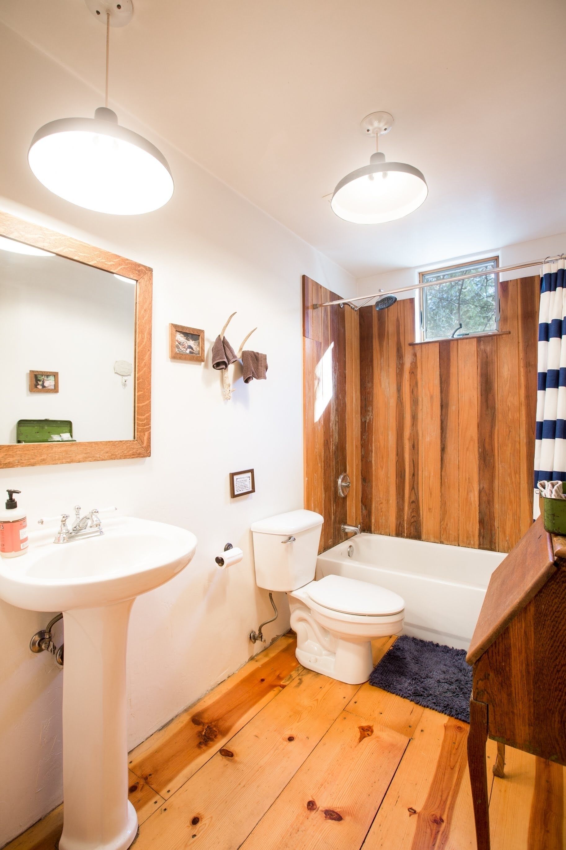 Une salle de bain avec un plancher en bois, des accessoires blancs, un grand miroir et un rideau de douche.
