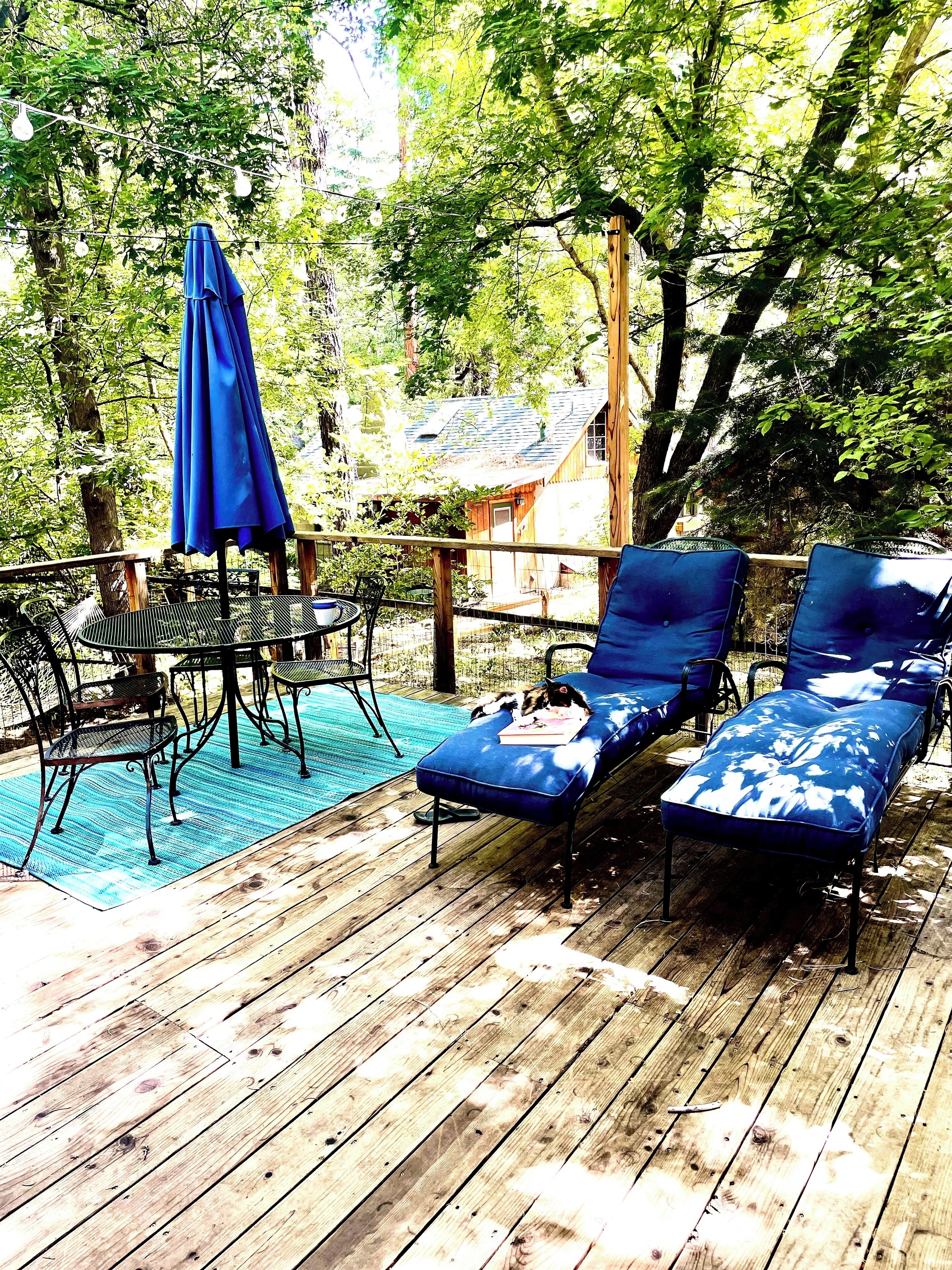 A wooden deck with lounge chairs and a table, surrounded by trees.