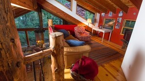 Interior acollidor d'una cabana amb sostre de fusta, un sofà amb coixins, una cadira vermella i una taula petita amb una làmpada.