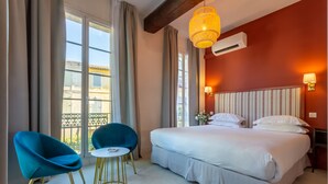 Ein Hotelzimmer mit einem großen Bett, zwei blauen Sesseln, einem kleinen runden Tisch und Blick ins Freie.