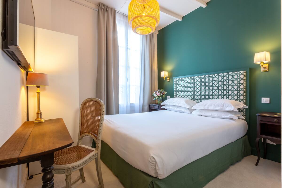 Une chambre d’hôtel équipée d’un lit, d’un bureau, d’une chaise, d’une lampe et d’un luminaire fixé au mur.