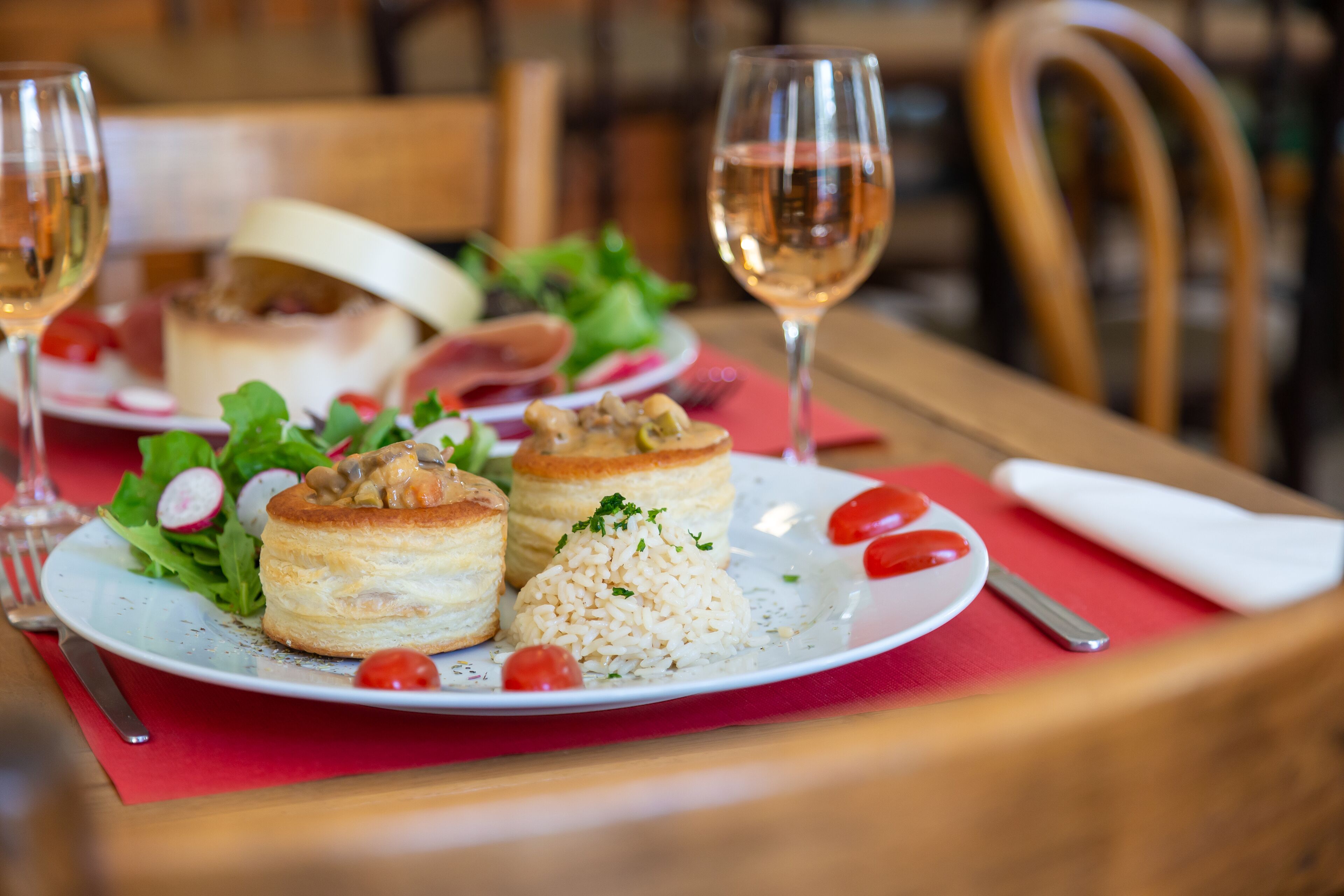 A plate of food with pastries, rice, and vegetables, accompanied by two glasses of white wine.