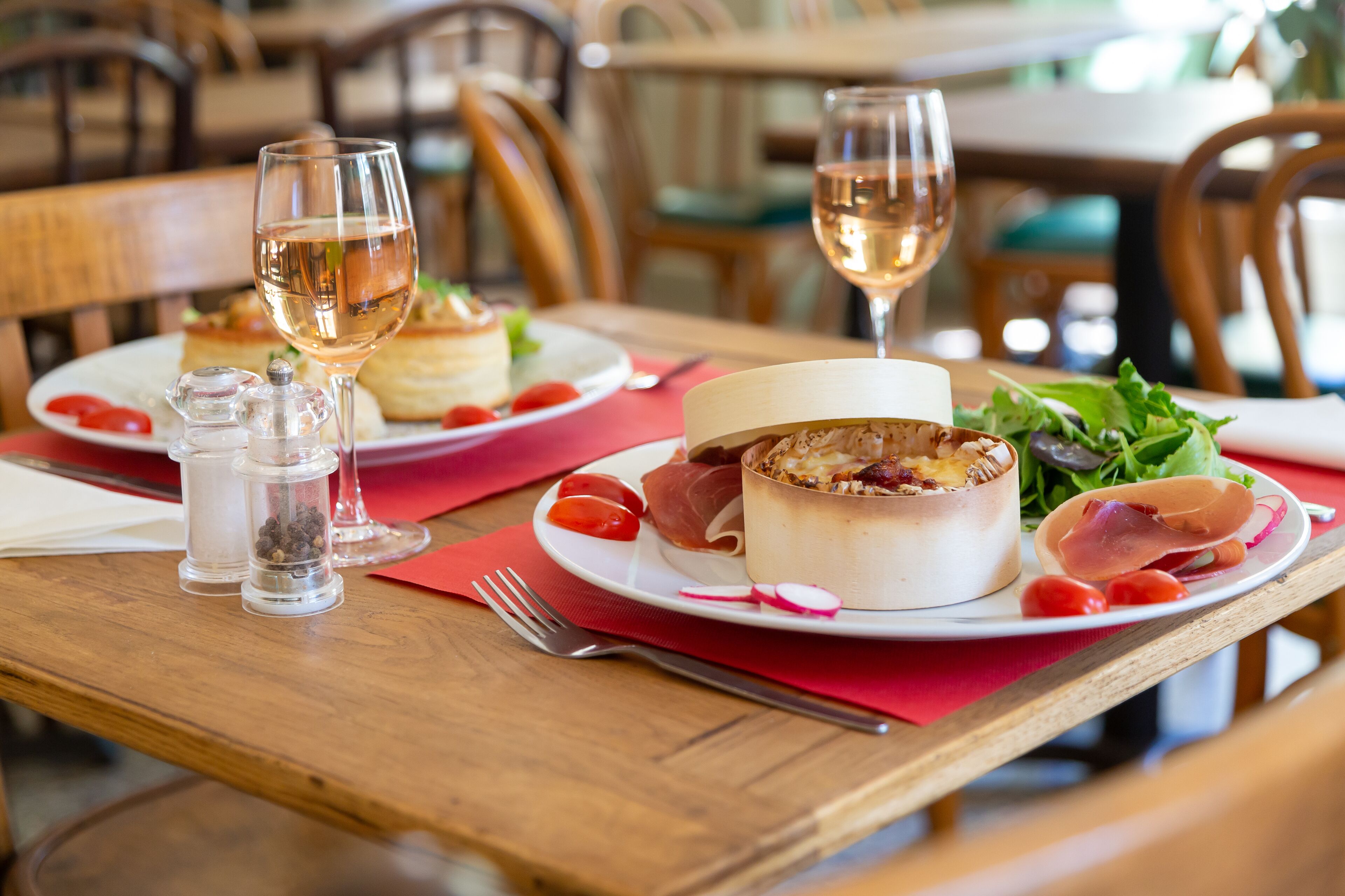 A dining table with plates of food, glasses of wine, and salt and pepper shakers.