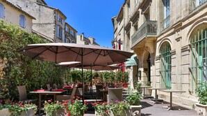 Ein Straßencafé mit Tischen und Sonnenschirmen, umgeben von Gebäuden im klassischen Stil.