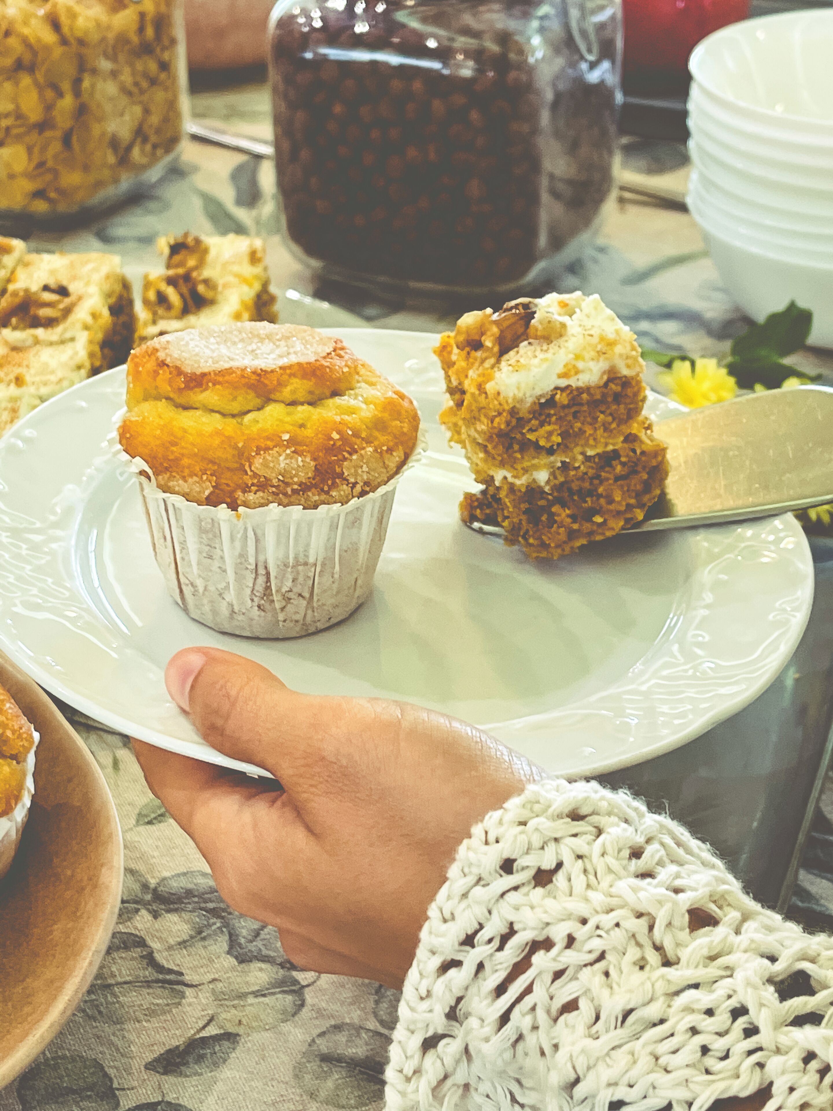 Una mano sosteniendo un plato con un muffin y una porción de pastel.