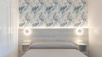 A bedroom with a patterned wallpaper, a bed with a herringbone quilt, and bedside tables with built-in lighting.