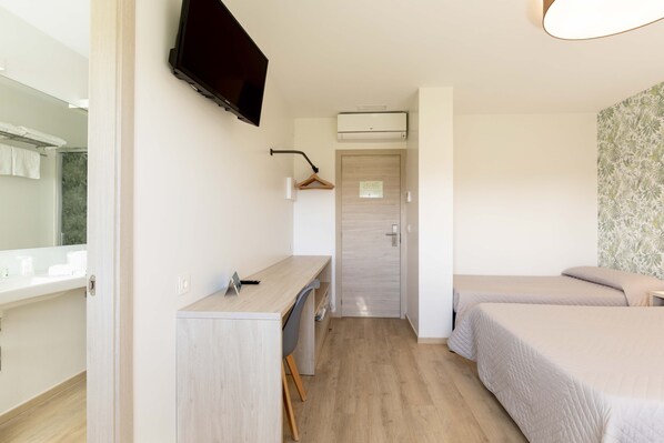 A hotel room with a desk, two beds, a TV, and an air conditioning unit.