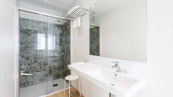 Un baño moderno con cabina de ducha de vidrio, un lavabo blanco y un taburete pequeño.
