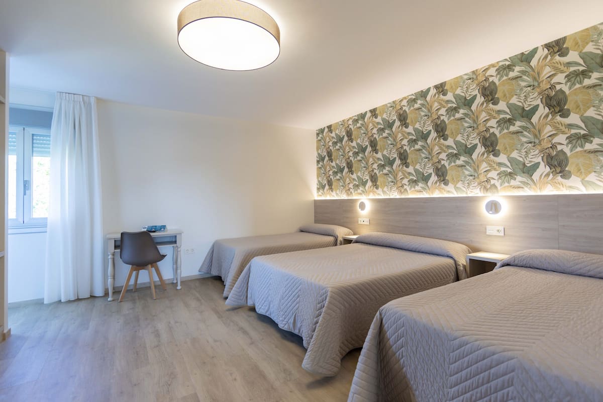 Quarto de hotel com três camas, uma escrivaninha e uma cadeira.