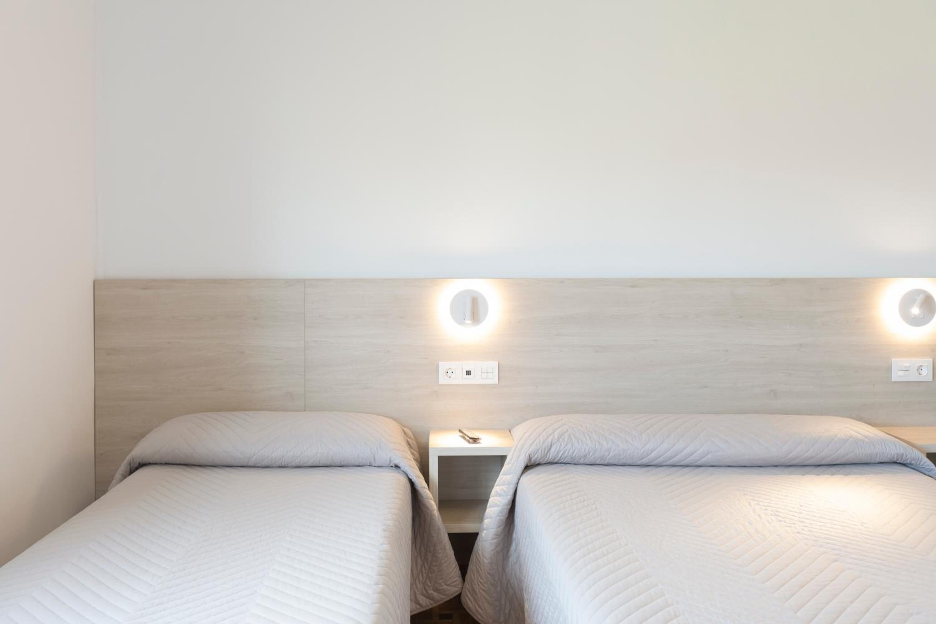 Habitación doble con dos camas individuales, cabecero de madera, lámparas de noche y una mesita entre las camas.