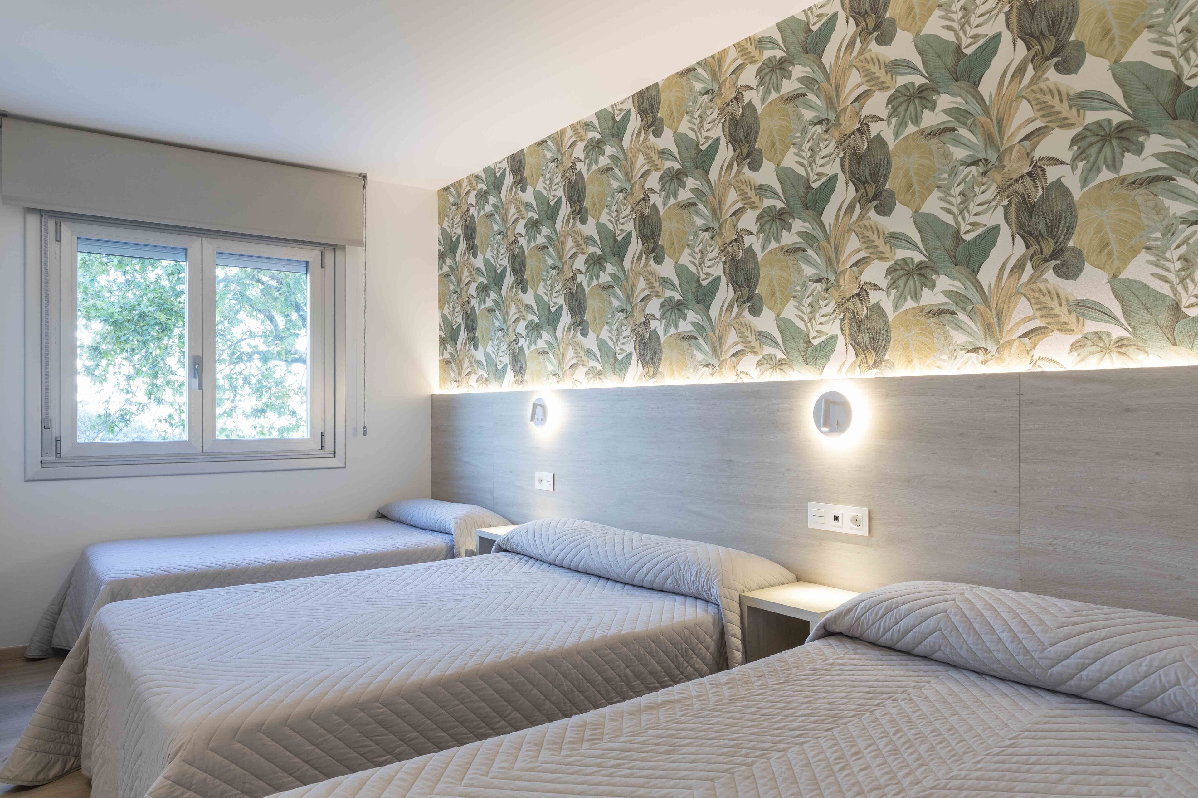 A hotel room with two beds, a large window, and a wall with a tropical leaf pattern.