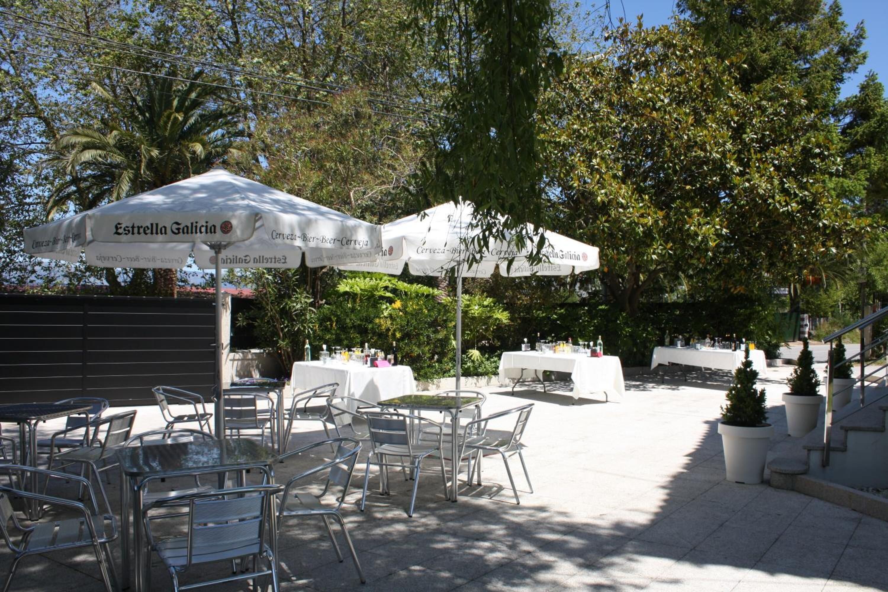 An outdoor patio area with tables and chairs, covered by white umbrellas, and surrounded by trees.