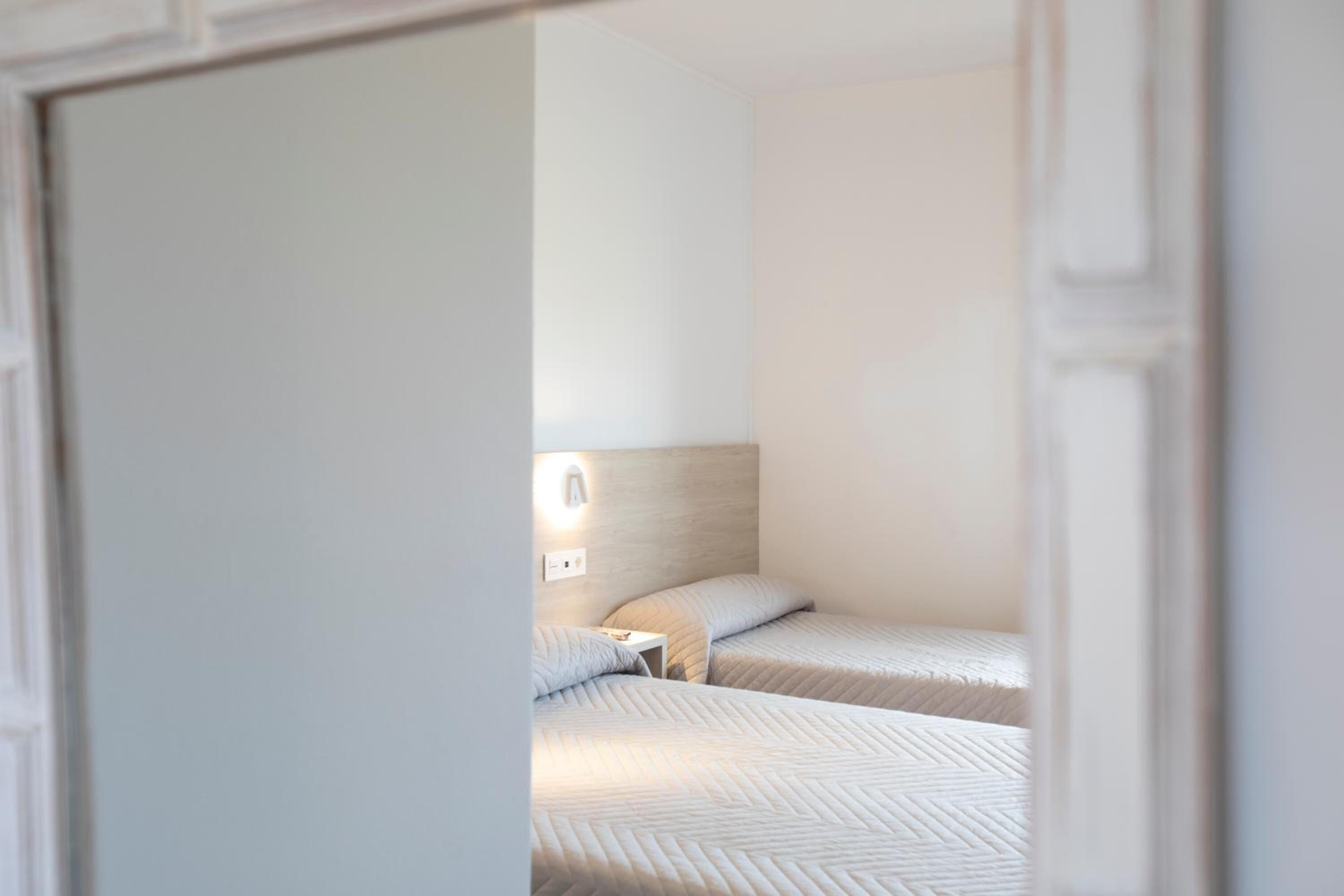Una habitación de hotel con dos camas, una mesita de noche y una lámpara fijada a la pared.