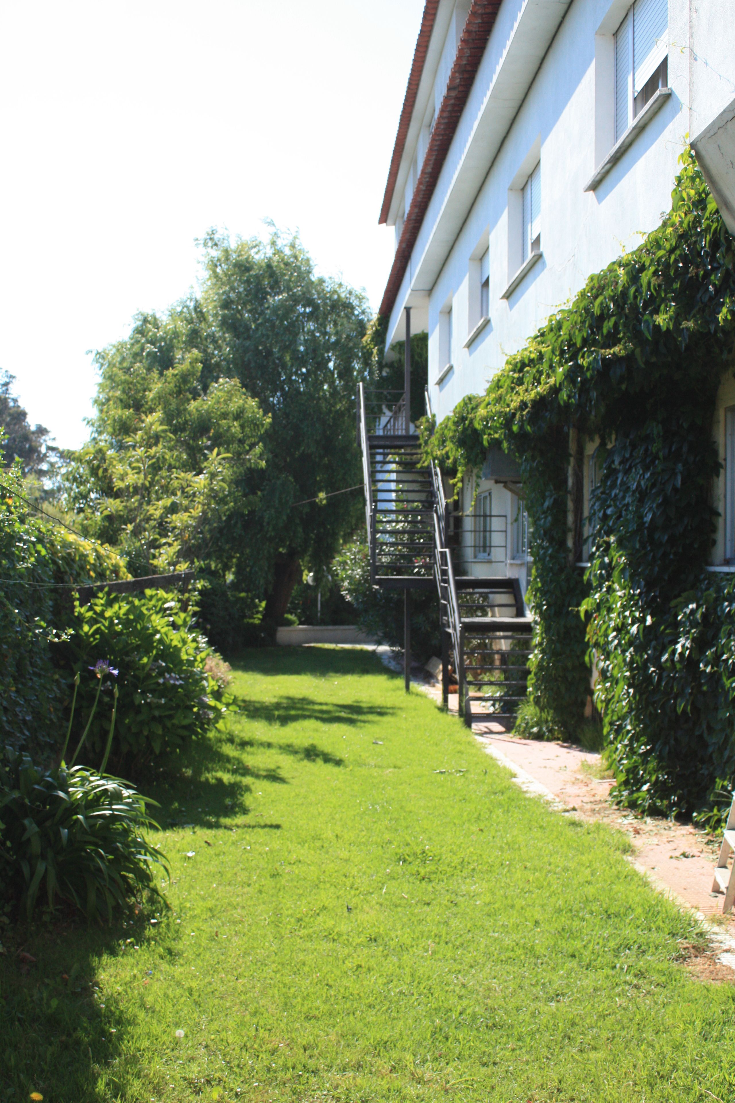 A building with a staircase leading to a door, surrounded by greenery and a well-maintained lawn.