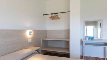 A bedroom with a bed, a bedside table, a wall-mounted shelf, a mirror, and a clothing rack.