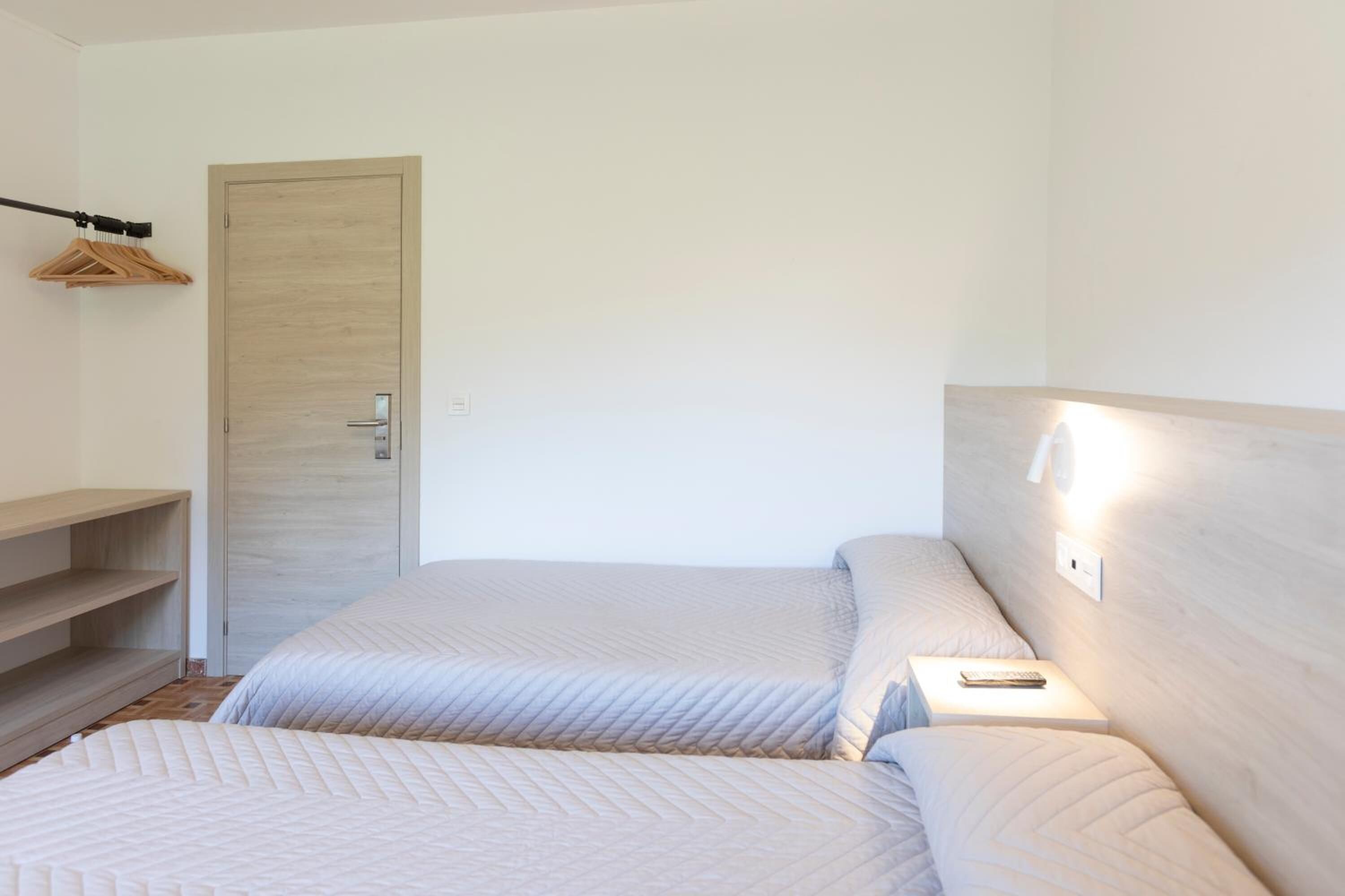 A room with two beds, a wooden door, a shelf, and a hanging coat rack.