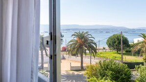A view from a window overlooking a coastal area with palm trees, a road, and boats on the water.
